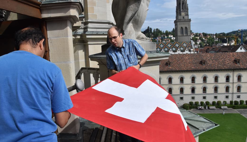 Die beiden Domsakristane, Roman Huber (hinten) und César Coronel, hissen die Schweizer Fahne zwischen den Türmen der Kathedrale St. Gallen. 