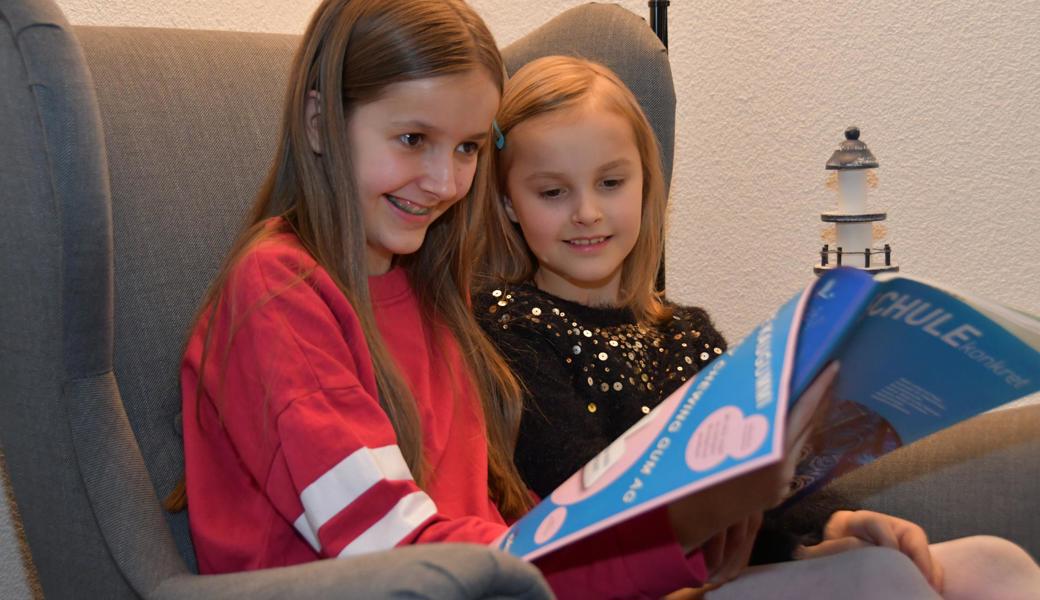 Anna Brunner (links) zeigt ihrer Schwester Mia die Ausgabe von «Schule konkret» (Nummer 8), in der das von ihr entworfene Inserat ganzseitig erschienen ist.