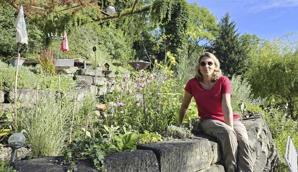 Mira Romer sitzt auf einer Trockensteinmauer in ihrem biodiversen Hanggarten. 