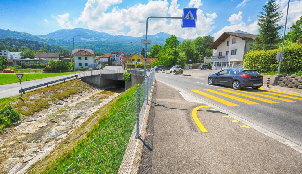 Die Rietstrasse (links vom Bach) ist zwar bereits vortrittsbelastet. Dennoch wird ein Trottoir drüber gezogen: Damit der Fussgängerstreifen rechts im Bild aufgehoben werden kann, wird der Geh- und Radweg über die Brücke und eben auch über die Rietstrasse verlängert.
