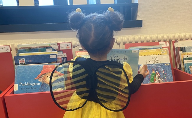 Ein Bienli stöbert in der Bibliothek bei den Kinderbüchern