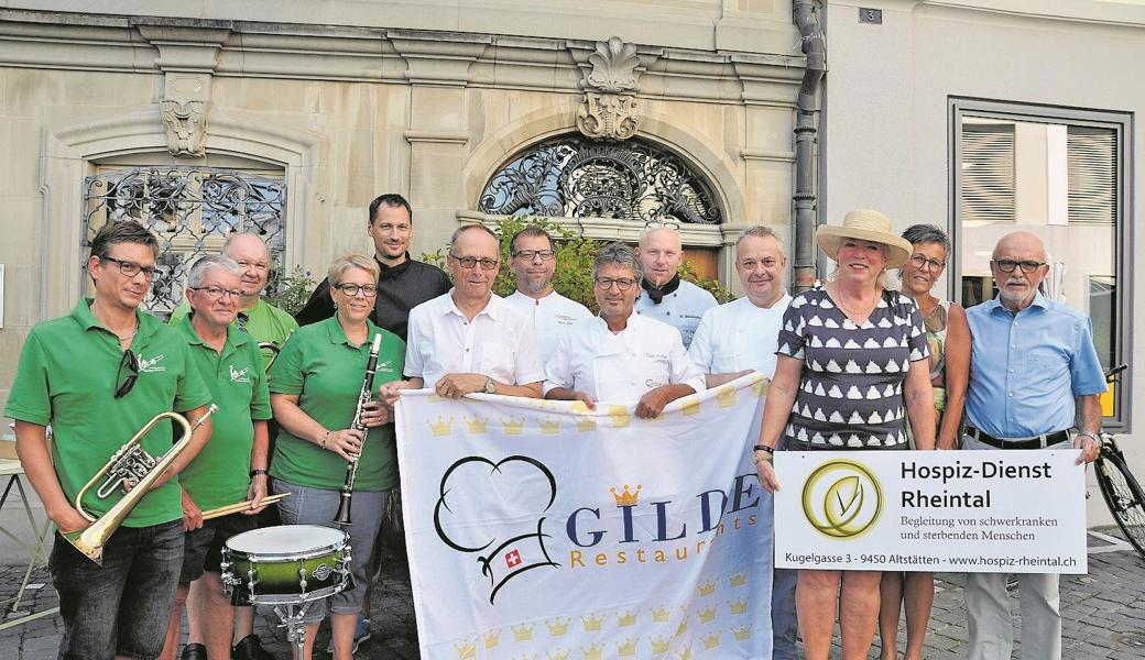 Links die Bauernkapelle Montlingen. Es kochen (v. l.) Kurt Indermaur (Maienhalde, Berneck), Gino Kobi (Landhaus, Rheineck), Fredi Koller (Grüntal, Altstätten), Dani Wildhaber (Adler, Oberriet), Peter Kast (Ochsen, Berneck). Daneben (v. l.) Jutta Cobbioni (Präsidentin), Regula Bont (Stellenleiterin) und Hans-Ruedi Büchel vom Hospiz-Dienst Rheintal. 