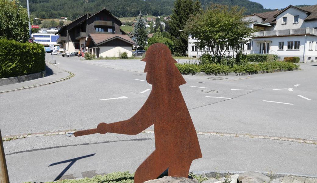 Hinter der Feuerwehrskulptur ist der Kiesplatz zu sehen, der sich als nahegelegener Abstellplatz für Autos anbietet. 