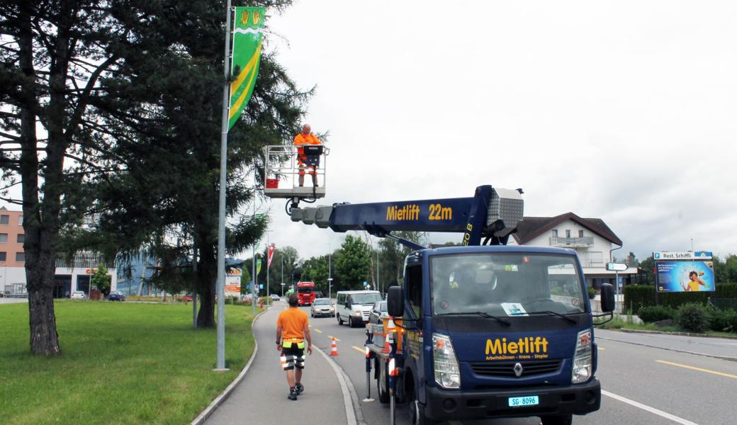 Gemeindemitarbeiter hängen die neuen Fahnen auf.